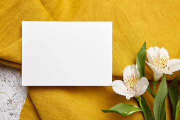 Top view of a landscape-oriented white card on mustard-colored fabric, complemented by white...