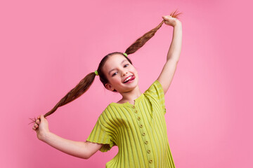 Photo portrait of cute little girl pulling tails stick tongue dressed stylish green clothes isolated on pink color background