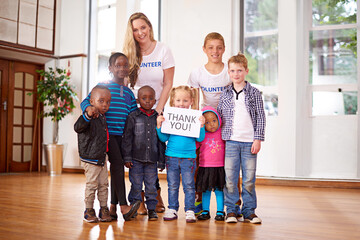 Children, volunteer and portrait at orphanage for donation, help and thank you sign for community service. Charity, kids and happy group with woman together at non profit ngo for support or gratitude