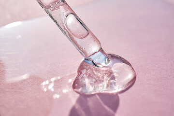 Pipette with serum shimmering in the sun on a pink background.