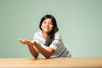 Happy Indian asian teenage girl showing or pointing something sitting at table