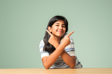 Happy Indian asian teenage girl showing or pointing something sitting at table