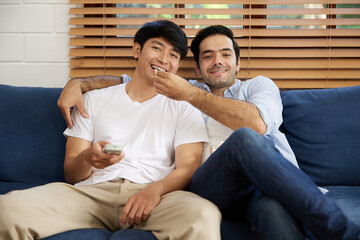 LGBT gay couple watching tv and eating popcorn in living room