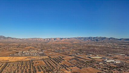 Las Vegas, NV, USA - May 11, 2024: Flying over brown wide desert landscape under blue morning sky SW from city. One-story house neighborhoods. Mountain range on horizon, 1 snow peak