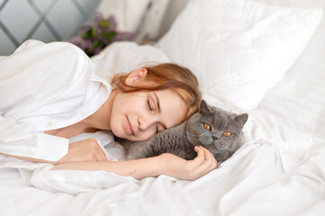 Yong teenager girl and gray cat sleeping together in bed, child and pet love and friendship