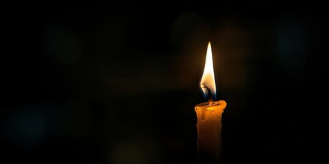 A single candle burning in darkness with negative space