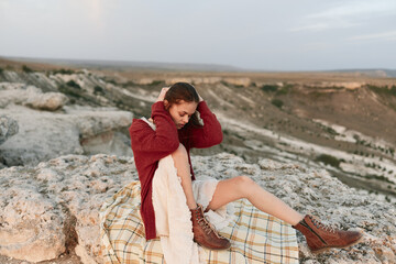 Fototapeta premium Woman sitting on edge of cliff in red sweater and brown boots, enjoying nature and adventure