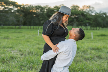 young latin couple in love in a field of green grass, man carrying his girlfriend