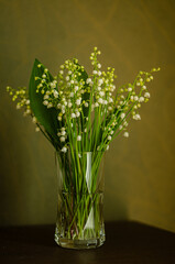 bouquet of white lily of the valley flowers in a glass vase, green background. High quality photo