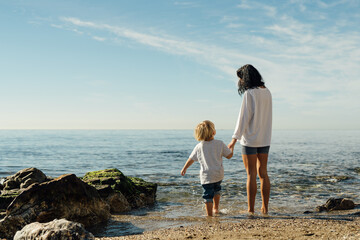 young mother and son stand on the seashore. A woman with a child stands on the beach, rest and...