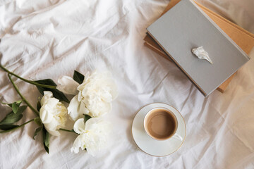 An inviting scene of a warm coffee cup and lush peonies on a bed, capturing the vibe of a relaxed...