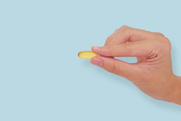 Children or teenager hand holding vitamin OMEGA-3 Fish Oil pill in fingers. Closeup studio shot isolated on light blue background. Concept of young human growth, heart and brain health, ADHD treatment