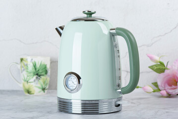 Modern electric kettle on kitchen table with cup and roses in background.