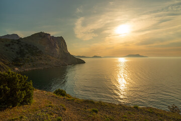 A beautiful sunset over the ocean with a mountain in the background. The sky is filled with clouds and the sun is setting. The water is calm and the sky is a mix of orange and pink hues.