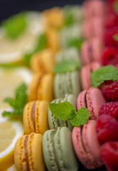 macaroons of different colors with with raspberries, lemon and mint