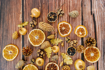 Cones, oak leaves, gold garnets, pieces of dried oranges lie on a wooden table. Top view