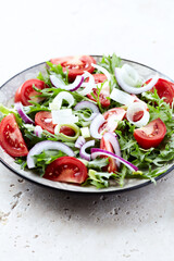 Salad with fresh tomatoes and arugula on a bright stone background. Close up. Copy space.	