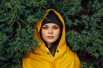 A mysterious young woman in a vibrant yellow raincoat hiding amidst lush evergreen trees in a...
