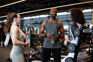 Waist up portrait of muscular African American man as fitness coach talking to two clients in gym...