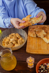 The hand of a Muslim woman breaks flatbread at a set table during the holiday of Eid al-Fitr