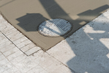 construction of a newly paved sidewalk with utility cover and shadow of a pole with traffic signals
