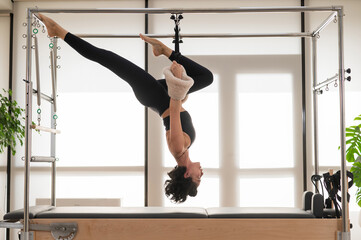 Asian woman doing aerial exercise on reformer machine. 