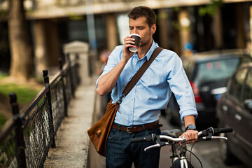 Smiling businessman with coffee and bicycle in urban setting