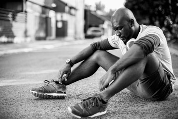 Black and white photo of active man sitting on street after workout outdoors