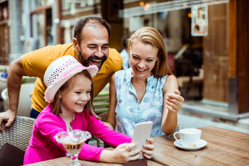 Happy family enjoying time together with smartphone at outdoor cafe