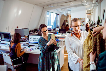 Female designer taking picture of finished product with colleagues in office