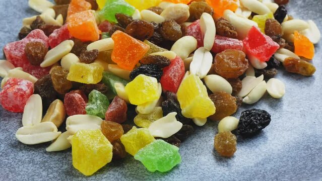 Mix of multi-colored candied fruits and nuts scattered on a gray surface, rotating in a circle. Medium plan