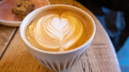 A cup of delicious golden flat white coffee with latte art heart on top on rustic wooden table in...