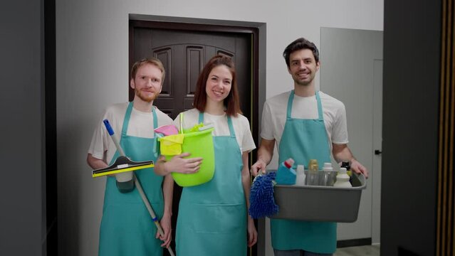Portrait of a trio of professional cleaners in a blue apron with various cleaning items cleaner and mop in a modern apartment cleaning on call