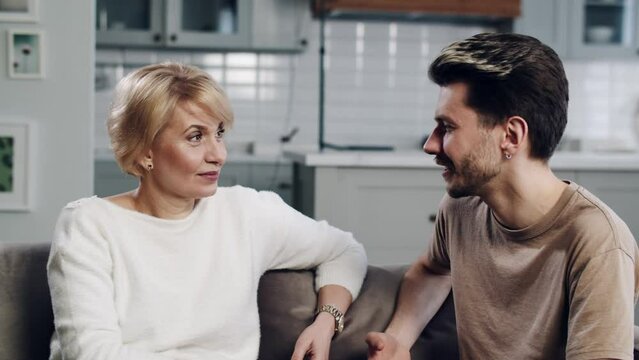 Concept of family reunion. An adult young son support his mature age single mother. Spend time with family. Mid shot adult man communicates with life experienced mature mom at home. Trust mom his