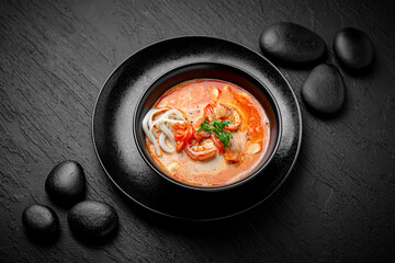 Composition of tom yam soup with shrimp and noodles on black background. The Art of Japanese...
