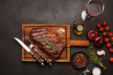 Grilled Striploin beef steak on wooden board with bottle and glass of red wine, vegetables, herbs...