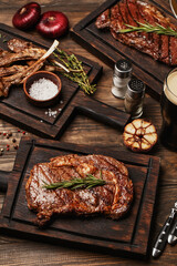 Wooden table served with various grilled meat, vegetables and glass of beer. Striploin steak,...