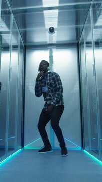 Young African American male IT specialist in headphones dancing in corridor of server room having fun