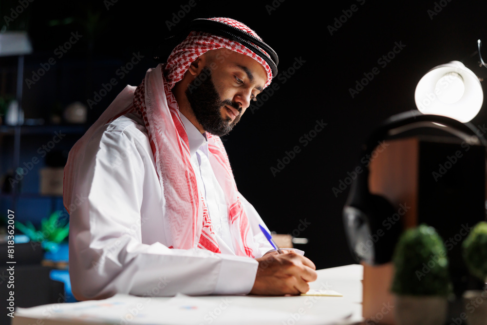 Aufkleber side-view of a focused male entrepreneur using his laptop while seated at a desk. arab guy focuses o