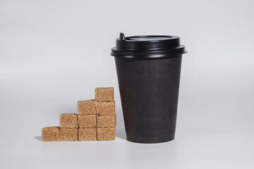 Dark brown paper coffee cup with black plastic lid and brown sugar cubes in the form of stairs....