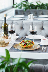 Restaurant table served with tableware, salad, glasses of red wine and bread basket. Fine dining. Restaurant interior