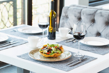 Restaurant table served with tableware, salad and glasses of red wine. Fine dining. Restaurant interior