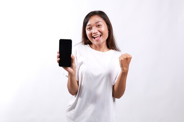 Excited young asian woman, showing smartphone app and triumphing, celebrating on mobile phone, standing over white background