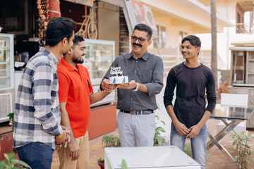 Tall, attractive man in dark shirt, glasses, accepts birthday cake, congratulations from friends.