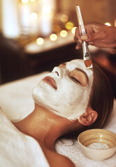 Woman, face mask and hand brush for spa treatment or beautician for vacation, stress relief or dermatology. Female person, calm and facial with candle bokeh at Bali resort in hotel, relax or skincare