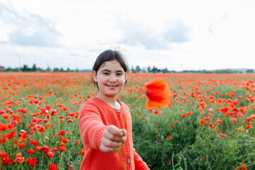 portrait of dark haired girl standing in the poppy field holding out the flower