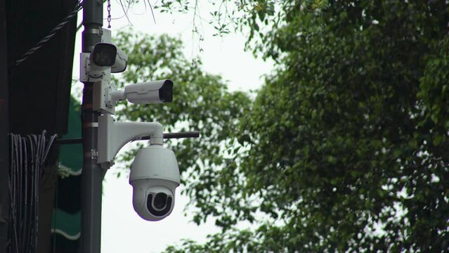 C&aacute;maras de seguridad callejeras blancas, arboles de fondo en un d&iacute;a nublado. Vigilancia. Cuatro c&aacute;maras de seguridad. C&aacute;mara de seguridad con movimiento giratorio. D&iacute;a nublado.