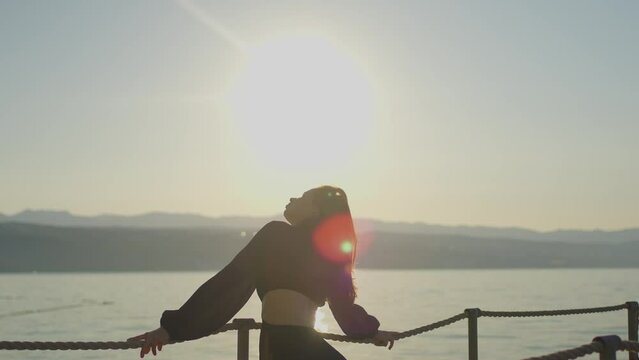 A woman happily gazes at the sunset over the ocean while standing on a pier