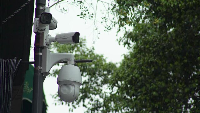 C&aacute;maras de seguridad callejeras blancas, arboles de fondo en un d&iacute;a nublado. Vigilancia. Cuatro c&aacute;maras de seguridad. C&aacute;mara de seguridad con movimiento giratorio. D&iacute;a nublado.