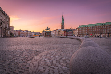 Copenhagen, a city square with a statue of a horse and a large building in the background. The sky is pink and orange, creating a warm and peaceful atmosphere